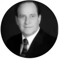 A black and white portrait of Rod Hess in a suit and tie, smiling gently against a dark background.